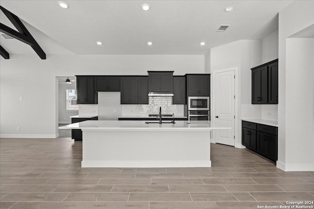 kitchen with a kitchen island with sink, sink, a textured ceiling, appliances with stainless steel finishes, and light hardwood / wood-style floors