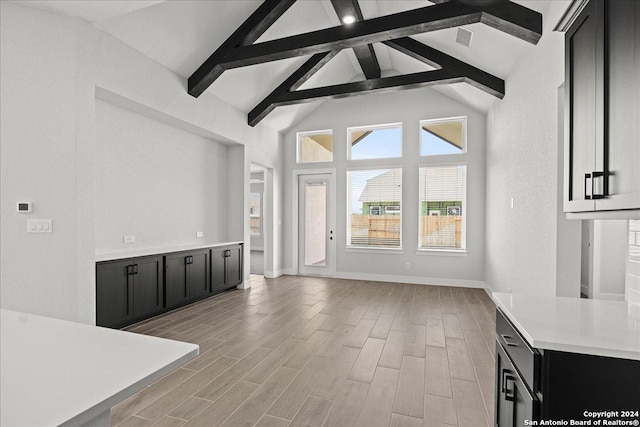 unfurnished living room with beam ceiling, high vaulted ceiling, and light wood-type flooring