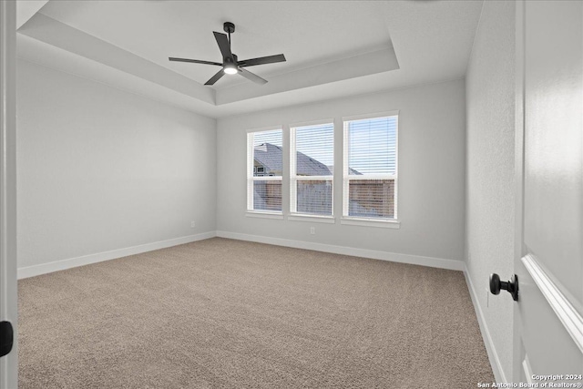 spare room with carpet floors, a tray ceiling, and ceiling fan