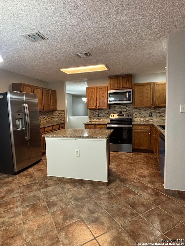 kitchen with a textured ceiling, stainless steel appliances, a kitchen island, and tasteful backsplash