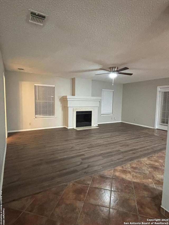 unfurnished living room featuring dark hardwood / wood-style floors, ceiling fan, and a textured ceiling