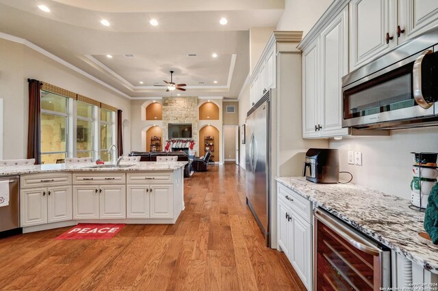 kitchen featuring sink, beverage cooler, stainless steel appliances, a tray ceiling, and light wood-type flooring