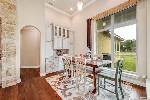 dining area with dark hardwood / wood-style flooring, ornamental molding, and a towering ceiling