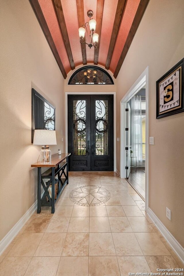 tiled entryway with vaulted ceiling with beams, a notable chandelier, and french doors