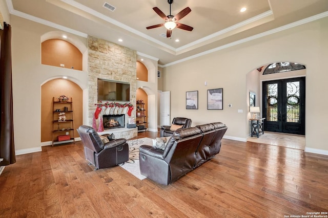 living room featuring french doors, light wood-type flooring, a stone fireplace, and ceiling fan