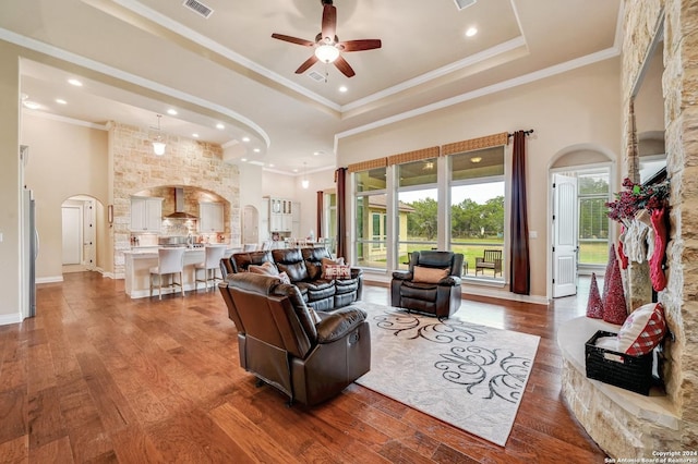 living room featuring a towering ceiling, ornamental molding, a tray ceiling, ceiling fan, and hardwood / wood-style floors