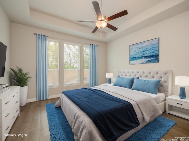 bedroom with dark hardwood / wood-style floors, ceiling fan, and a tray ceiling