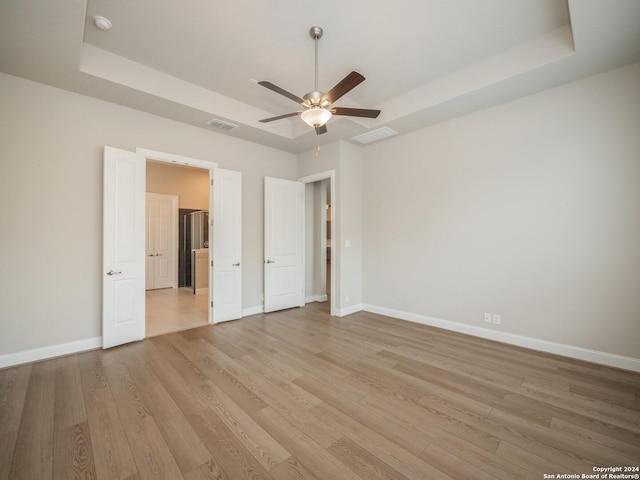 unfurnished bedroom featuring ceiling fan, a raised ceiling, and light hardwood / wood-style flooring