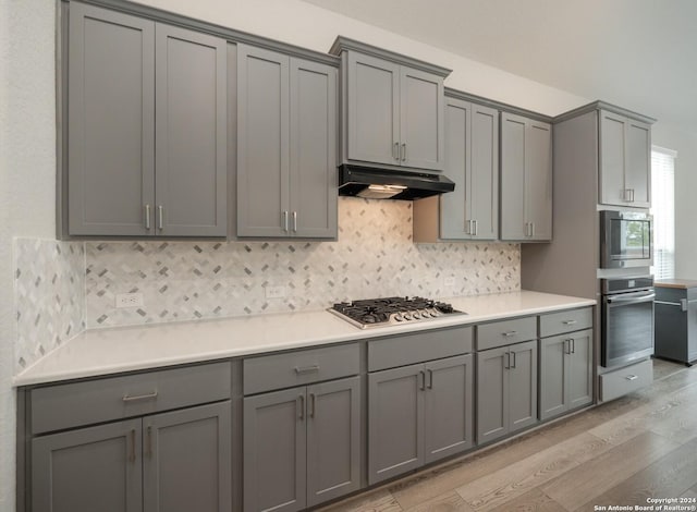 kitchen featuring gray cabinets, stainless steel appliances, light hardwood / wood-style flooring, and tasteful backsplash