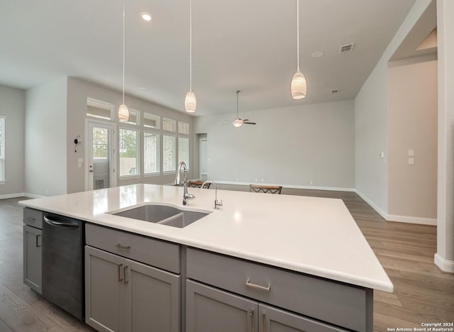 kitchen featuring dishwasher, a center island with sink, sink, gray cabinets, and light wood-type flooring