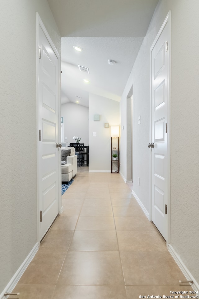 hallway with light tile patterned floors and lofted ceiling