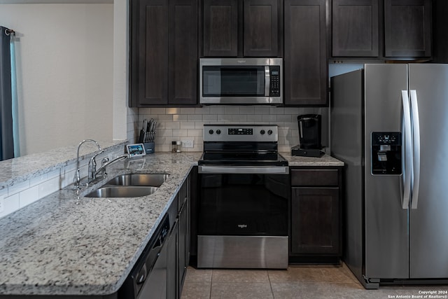 kitchen with sink, tasteful backsplash, light stone counters, light tile patterned floors, and appliances with stainless steel finishes