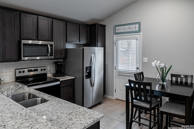 kitchen featuring sink, vaulted ceiling, decorative backsplash, light stone countertops, and stainless steel appliances