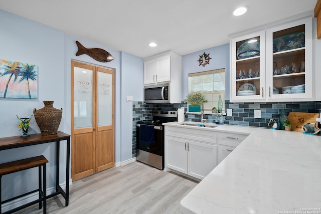 kitchen featuring light wood-type flooring, tasteful backsplash, light stone counters, stainless steel appliances, and white cabinets