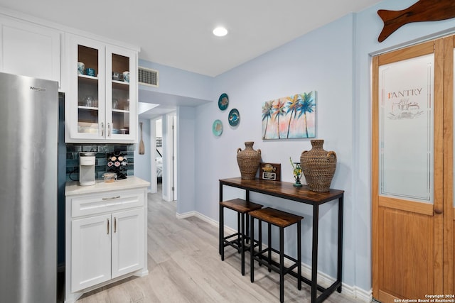 kitchen featuring white cabinetry, decorative backsplash, stainless steel fridge, and light wood-type flooring