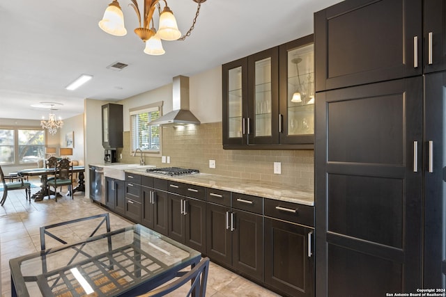 kitchen featuring pendant lighting, wall chimney range hood, stainless steel appliances, and an inviting chandelier