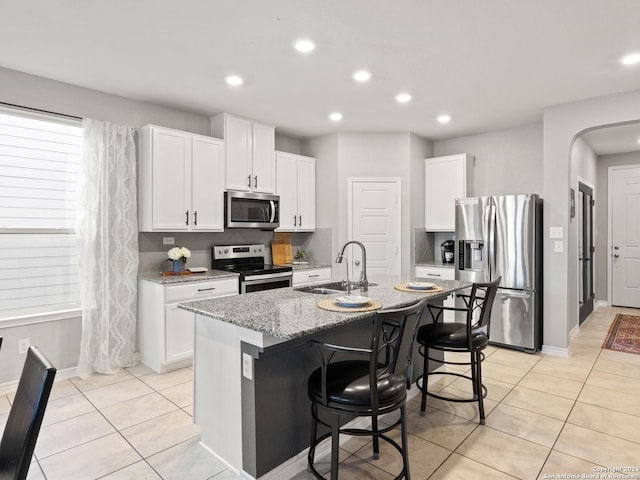 kitchen featuring white cabinets, light stone countertops, a kitchen island with sink, and appliances with stainless steel finishes