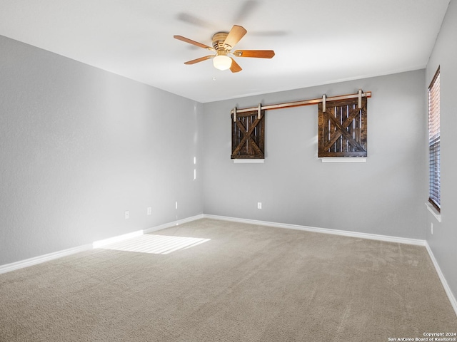 unfurnished room with a barn door, ceiling fan, and carpet