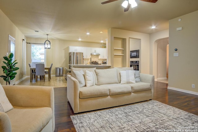 living room with hardwood / wood-style floors, ceiling fan with notable chandelier, and built in features