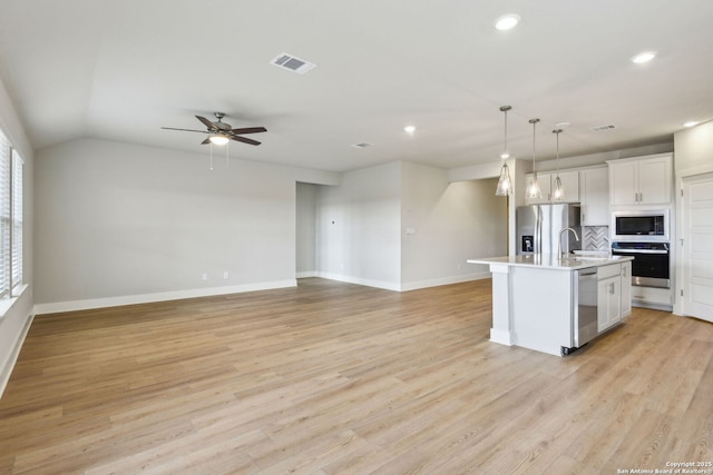 kitchen featuring pendant lighting, stainless steel appliances, light hardwood / wood-style floors, white cabinets, and a center island with sink