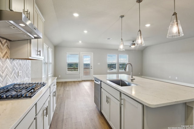 kitchen featuring sink, light stone counters, stainless steel appliances, a kitchen island with sink, and backsplash