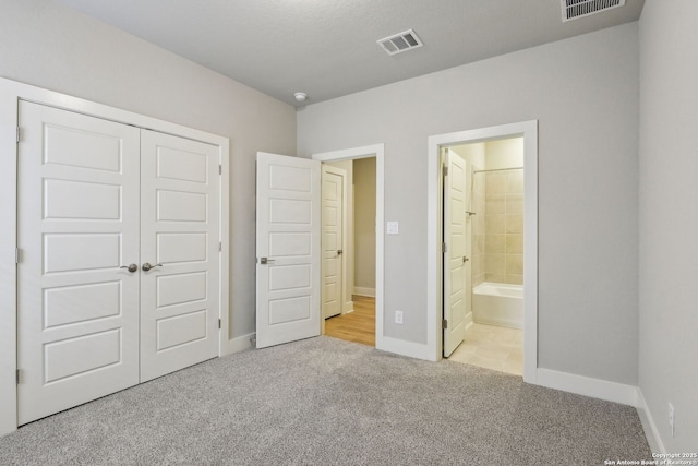 unfurnished bedroom featuring light colored carpet, ensuite bathroom, and a closet