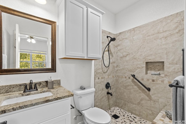 bathroom with vanity, ceiling fan, toilet, and tiled shower