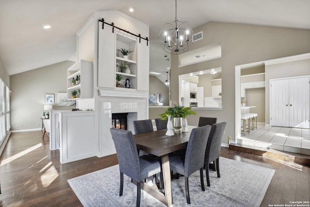 dining area featuring a chandelier, a barn door, dark hardwood / wood-style floors, and a large fireplace