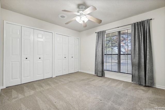 unfurnished bedroom featuring light carpet, ceiling fan, and multiple closets