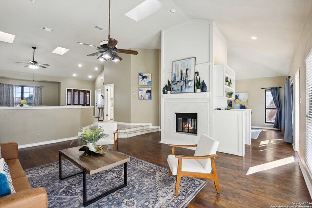 living room featuring high vaulted ceiling, a skylight, ceiling fan, a fireplace, and dark hardwood / wood-style flooring