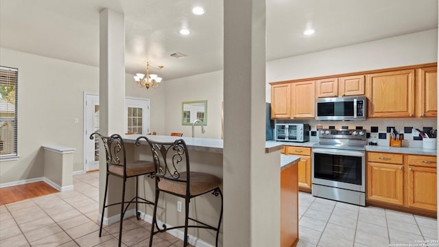 kitchen with decorative backsplash, a kitchen bar, stainless steel appliances, a chandelier, and light tile patterned flooring