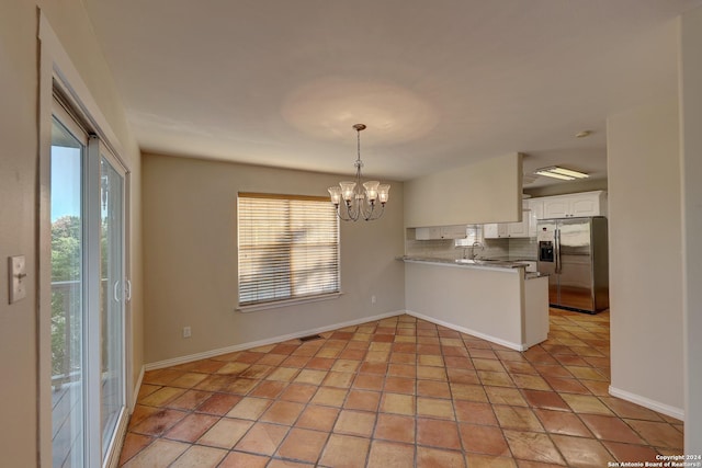 kitchen with kitchen peninsula, stainless steel refrigerator with ice dispenser, decorative backsplash, white cabinets, and a chandelier