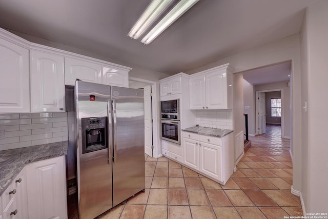 kitchen with white cabinets, appliances with stainless steel finishes, tasteful backsplash, and dark stone countertops