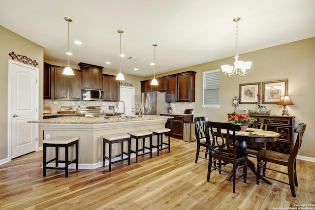 kitchen featuring stainless steel appliances, hanging light fixtures, and light hardwood / wood-style flooring