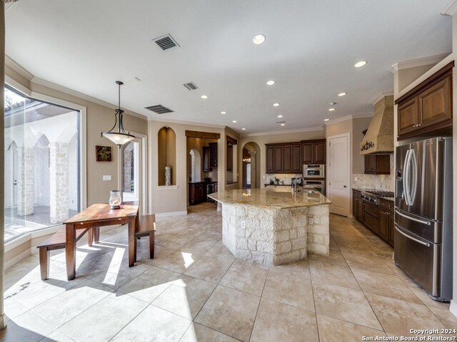 kitchen featuring arched walkways, visible vents, custom range hood, a kitchen island with sink, and stainless steel appliances