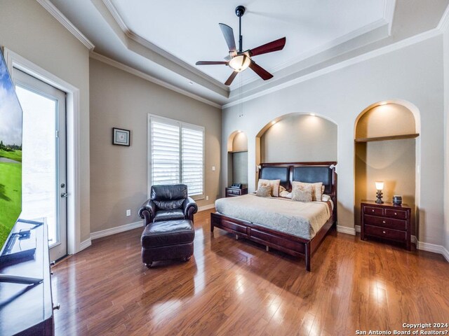 bedroom with baseboards, wood finished floors, access to exterior, a tray ceiling, and crown molding