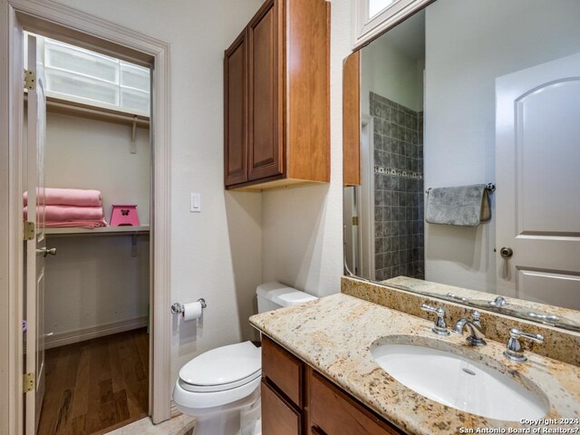 full bathroom with tiled shower, vanity, toilet, and wood finished floors