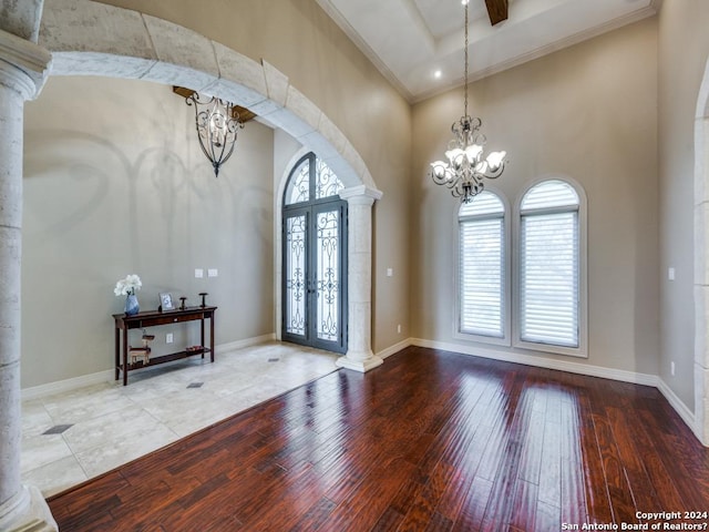 foyer featuring arched walkways, wood-type flooring, a notable chandelier, and decorative columns