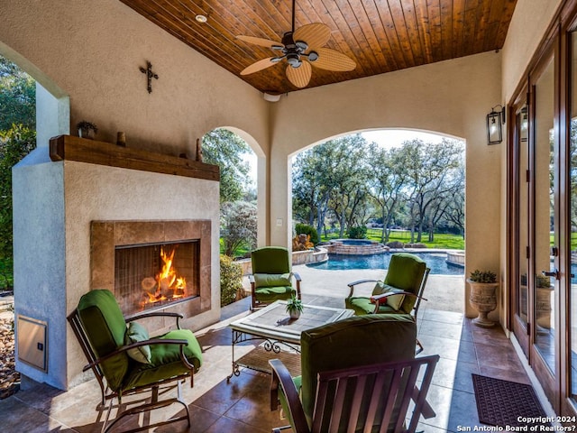 view of patio featuring ceiling fan, a lit fireplace, and a pool with connected hot tub