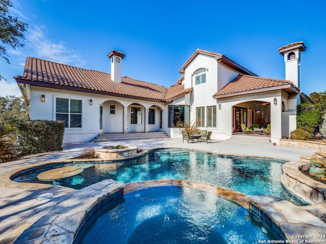 back of house featuring a pool with connected hot tub, a tiled roof, stucco siding, a chimney, and a patio area