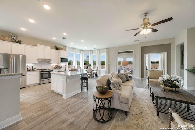 kitchen with appliances with stainless steel finishes, a breakfast bar, white cabinetry, an island with sink, and backsplash