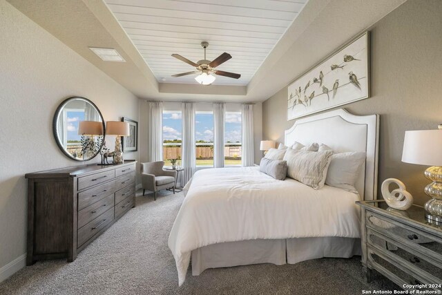 bedroom with a raised ceiling, ceiling fan, and light colored carpet