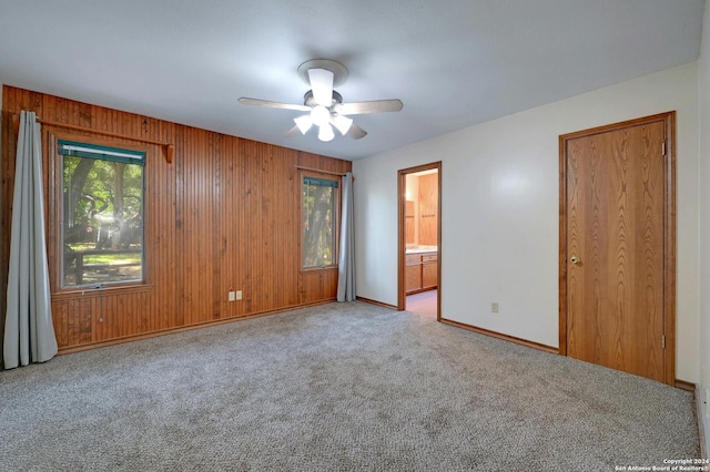 unfurnished bedroom with ceiling fan, wood walls, light carpet, and ensuite bath