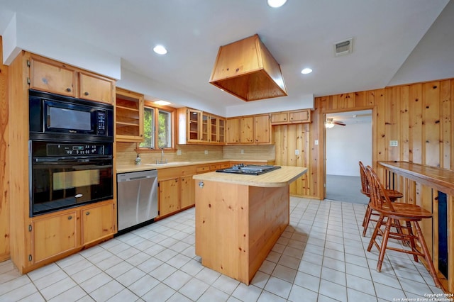 kitchen with ceiling fan, wooden walls, black appliances, light tile patterned floors, and a center island