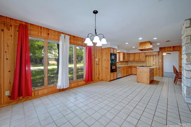 kitchen featuring wood walls, a center island, black appliances, and decorative light fixtures