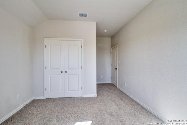 unfurnished bedroom with a closet, light colored carpet, and lofted ceiling