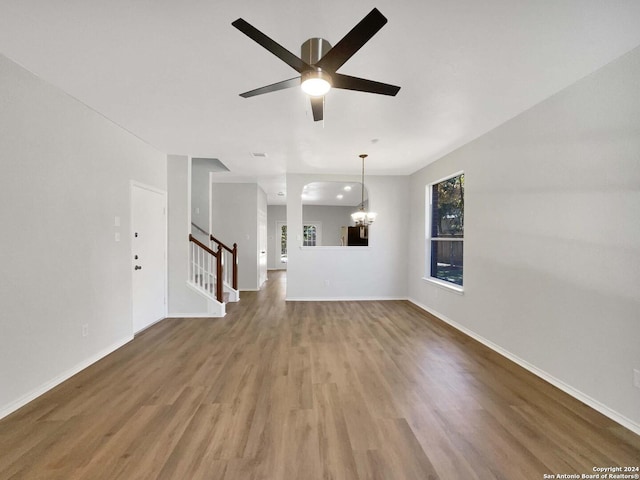 unfurnished living room featuring ceiling fan with notable chandelier and hardwood / wood-style flooring