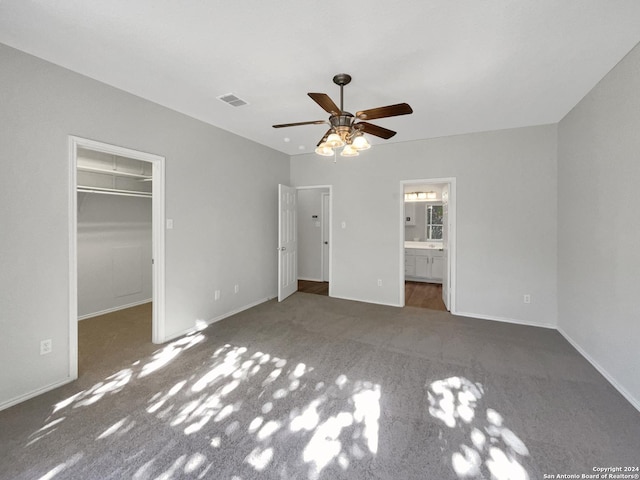 unfurnished bedroom with a walk in closet, ceiling fan, a closet, and dark colored carpet