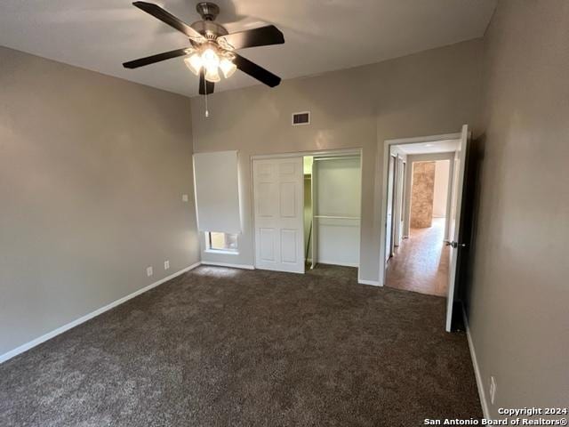 unfurnished bedroom with ceiling fan, dark carpet, a towering ceiling, and a closet