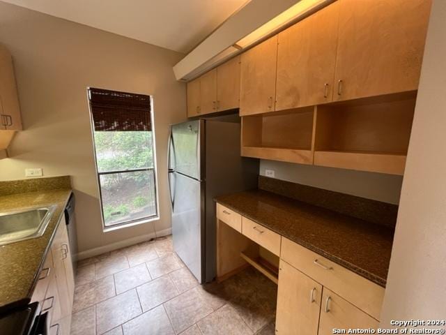 kitchen with dark stone countertops, stainless steel fridge, sink, and light tile patterned floors